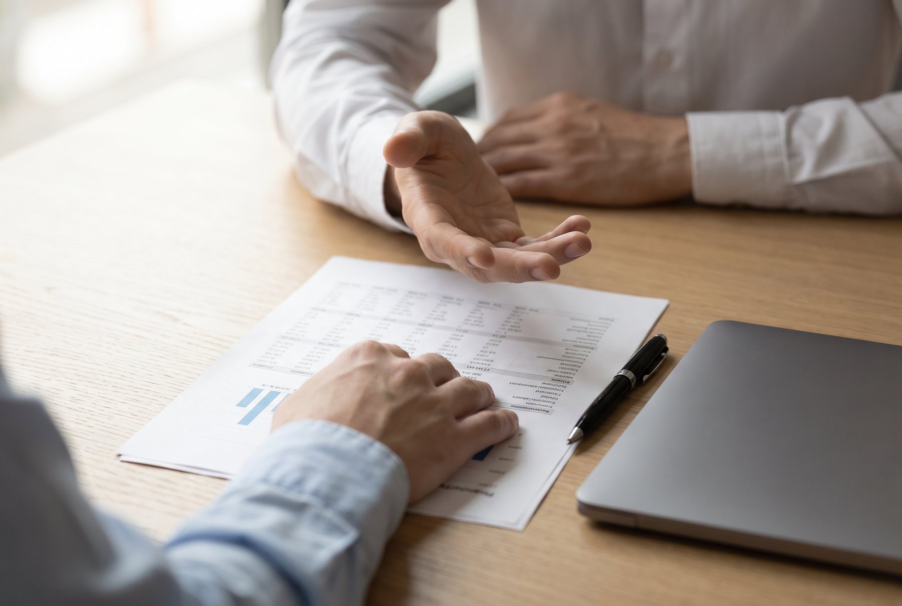 Two advisers and a client reviewing a printed set of accounts across a table, hands and documents in frame